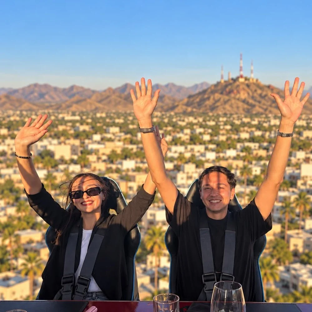 Pareja celebrando con los brazos en alto, vista de Hermosillo al atardecer