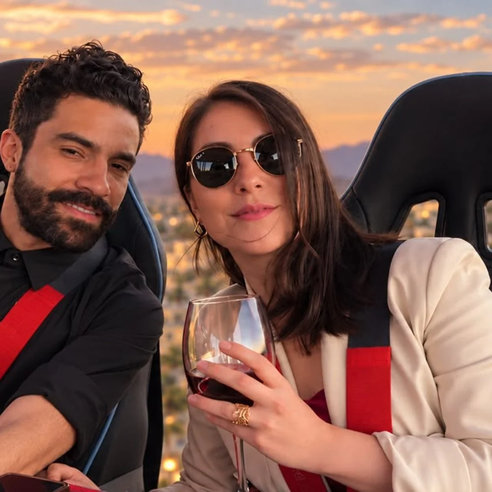 Pareja disfrutando copas de vino tinto con la puesta de sol de fondo